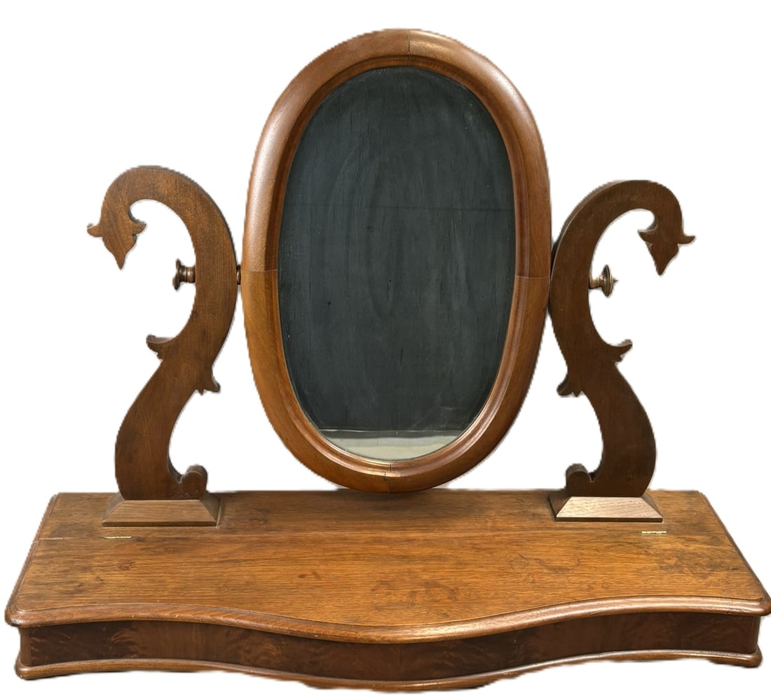 Antique Victorian Walnut Shaving Mirror Stand Serpentine Base: Antique Victorian period walnut shaving mirror featuring an oval swivel mirror mounted between decorative carved scroll supports above a shaped serpentine base with integrated storage compartment. The