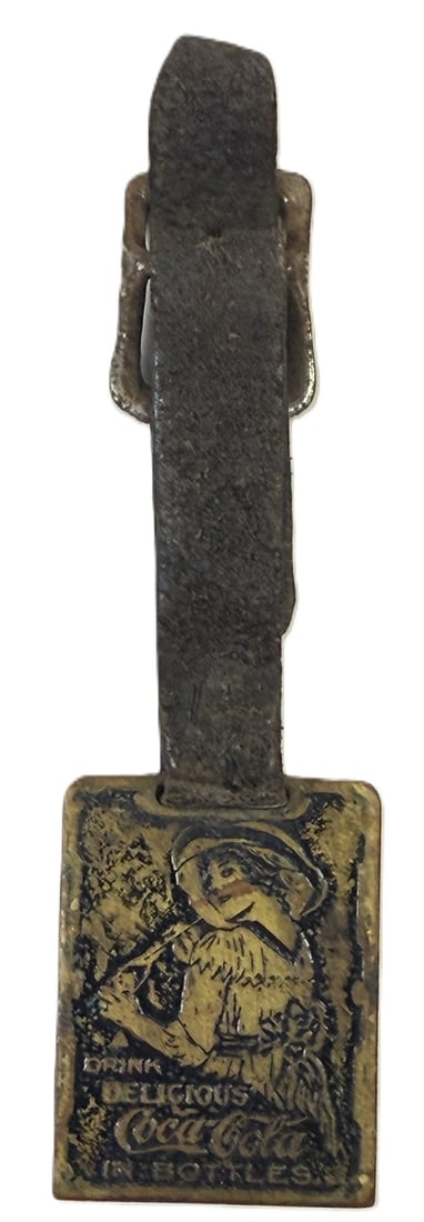 Drink Delicious Coca Cola In Bottles Original 1900s Brass Leather Key Fob: Vintage Coca-Cola advertising fob featuring the text 'Drink Delicious Coca-Cola in Bottles' and an embossed image of a woman in period attire. The fob is constructed of metal with a worn finish, and t