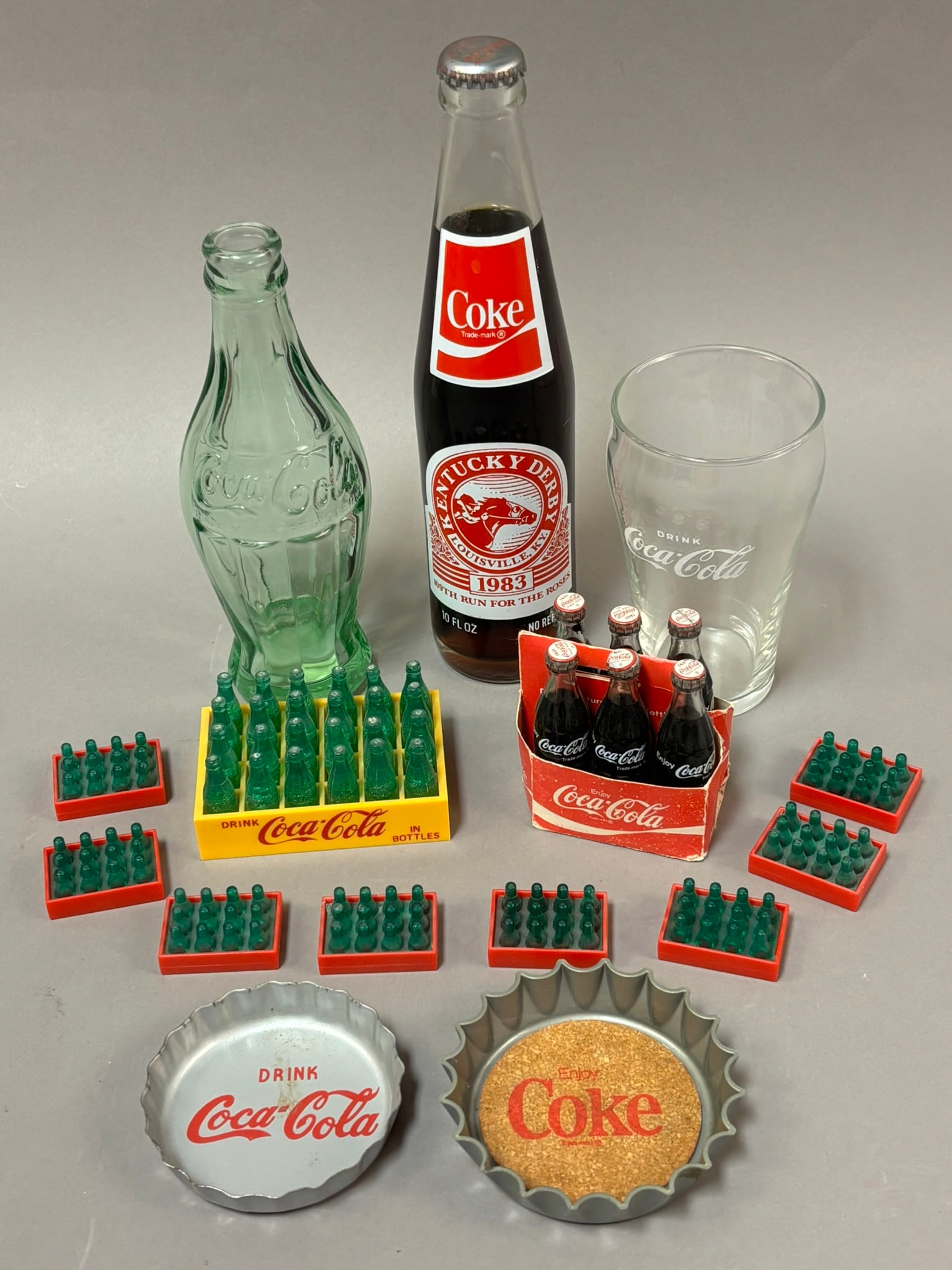 Lot 15 Vintage Coca Cola Advertising Miniature Bottles Caps & More: Mixed lot of Coca-Cola collectibles including a sealed 1983 Kentucky Derby Louisville KY commemorative 10 oz Coke bottle with original cap and contents, a clear Coca-Cola script drinking glass, a larg