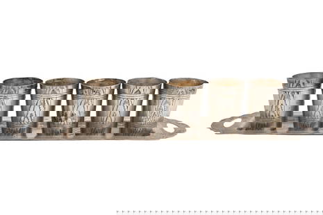 A SET OF SIX RUSSIAN WHITE METAL SHOT GLASSES ON AND TRAY Russia, circa 1900: A SET OF SIX RUSSIAN WHITE METAL SHOT GLASSES AND A TRAY Russia, circa 1900 Each with a flared body decorated with panels of pattern imitating woodgrain, the long rectangular tray similarly