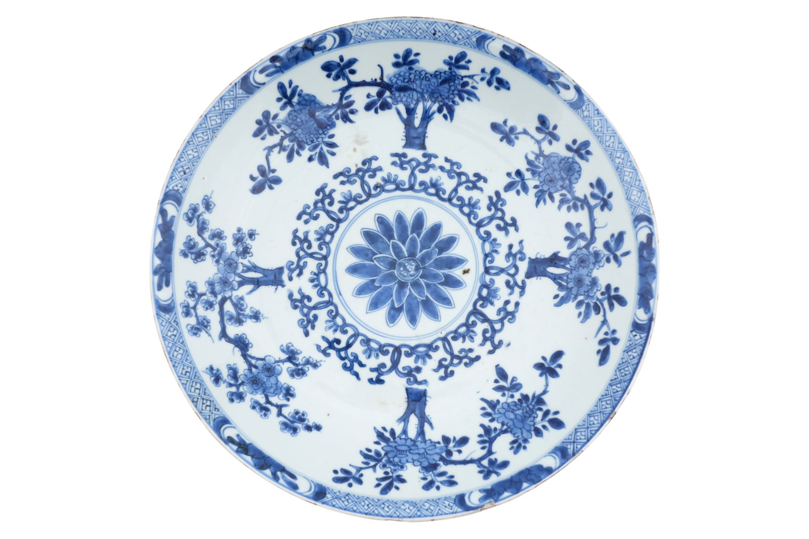 A LARE CHINESE BLUE AND WHITE CHARGER Kangxi period: A LARE CHINESE BLUE AND WHITE CHARGER Kangxi period Painted with a central lotus blossom surrounded by arabesques of tendrils and blooming trees, the rim with panels of peaches on a diaper ground, the