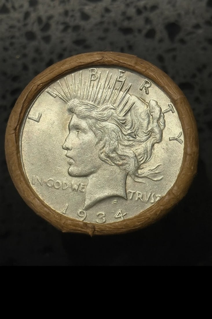 BU $10 Peace Silver Dollar Roll 1934 & 1922 Ends: An original Brilliant Uncirculated (BU) sealed roll containing 10 Peace Silver Dollars, featuring a 1934 coin on one end and a 1922 coin on the other. The roll remains sealed to ensure the interior co