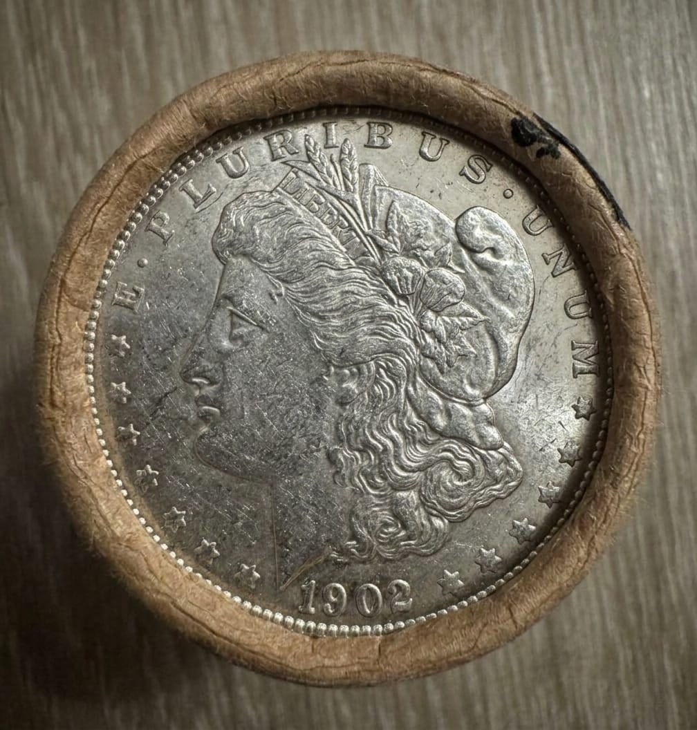 AU $10 Morgan Silver Dollar Roll 1902 & CC Ends: Sealed $10 AU Morgan Dollar roll featuring an 1902 coin on one end and a Carson City (CC) mint example on the other. Interior coins are unexamined due to sealed format. Light wear consistent with AU g