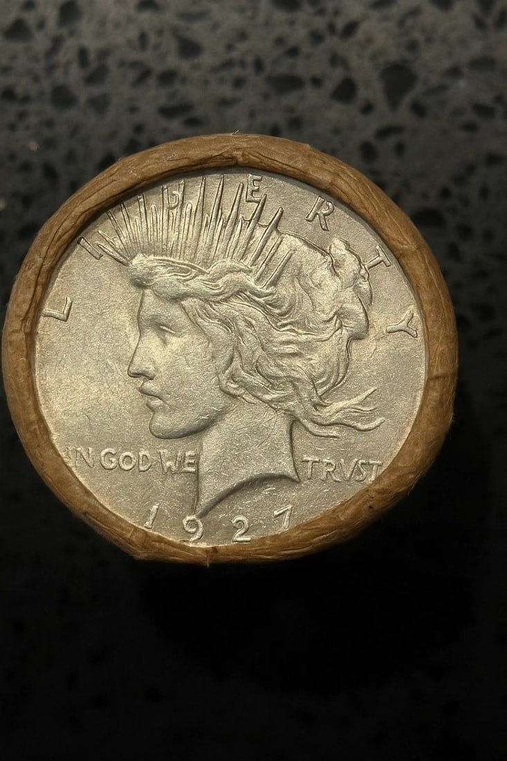 BU $20 Peace Silver Dollar Roll 1927 & 1922 Ends: An original Brilliant Uncirculated (BU) sealed roll of Peace Silver Dollars, featuring a 1927 coin on one end and a 1922 coin on the opposite end. The roll remains sealed with only the end coins visib