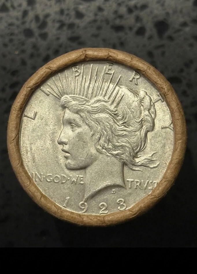 BU $10 Peace Silver Dollar Roll 1923 & 1927 Ends: An original Brilliant Uncirculated (BU) sealed roll containing 10 Peace Silver Dollars, featuring a 1923 coin on one end and a 1927 coin on the other. The roll remains sealed to ensure the interior co