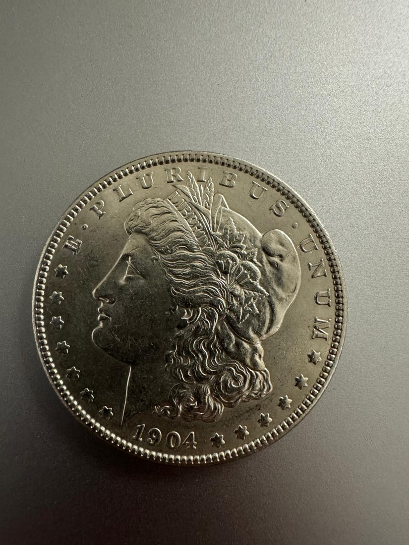 1904-P Morgan dollar AU: The 1904-P Morgan Dollar AU (Non-Graded) is a late-date Morgan Dollar struck at the Philadelphia Mint (no mintmark). In About Uncirculated condition, it shows only slight wear on high points with trac
