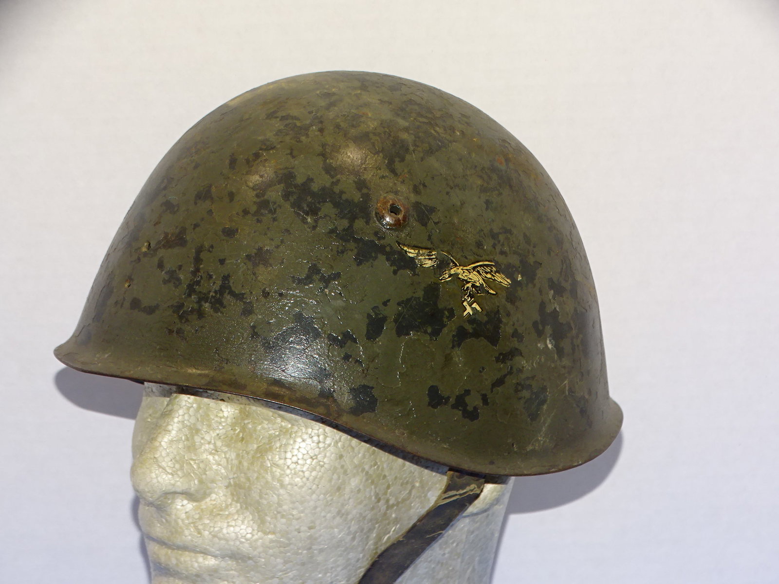 WWII Italian / German Luftwaffe Re-Issue Helmet: INTERESTING WWII ITALIAN HELMET THAT WAS RE-ISSUED FOR USE BY THE LUFTWAFFE. LUFTWAFFE DECAL TO ONE SIDE SHOWS SOME WEAR AND LOSSES AS DOES THE GREEN PAINTED FINISH, LINER AND CHIN STRAP ARE PRESENT A