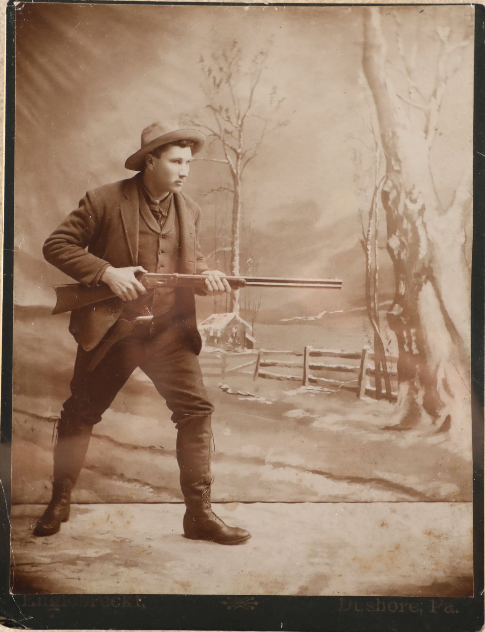 Antique 1890s Englebreckt Dushore, PA "Dude" W/ Winchester 1886 Lever Rifle 8.5" x 6.5" Cabinet Card: Good Condition. Some scattered scuffing to the corners. Shrink wrapped to a poster board backing. Features a great image of a young "dude" packing a pistol and holding a Winchester 1886 lever action r