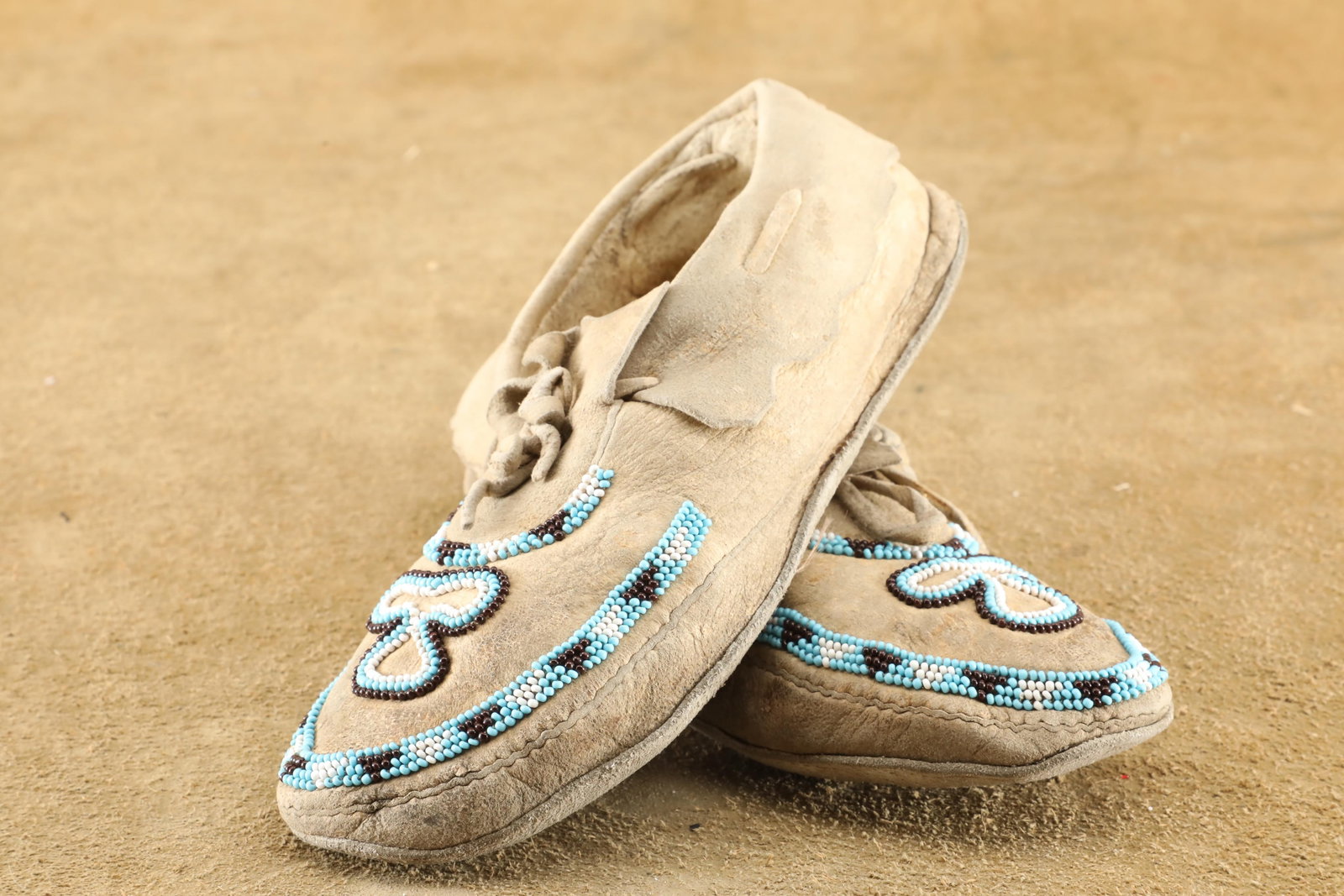 Antique 20th Century Plains Indians Beaded Deerskin Moccasins: Good Condition. Some scattered darkening throughout. They feature exquisite brown, turquoise, and white bead-work at the toes and insteps, boast stitched construction throughout, and measure about 10"