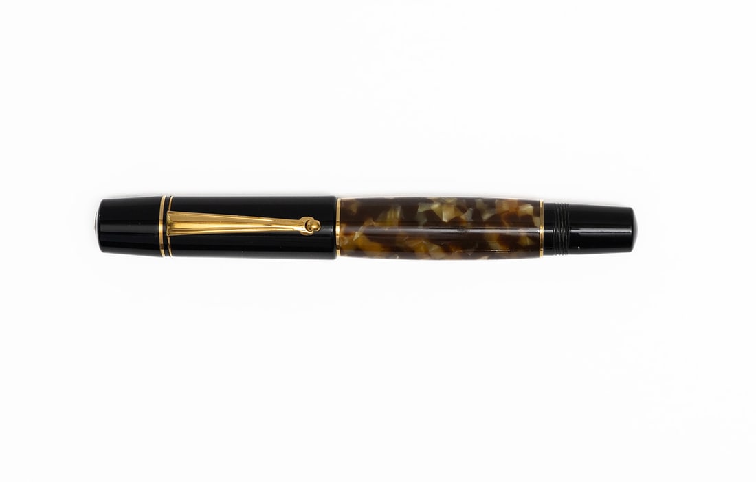 Delta Parthenope Honey Brown Marble Fountain Pen: Delta Parthenope tortoiseshell brown marble fountain pen. Honey brown colour marbled barrel with black clip and gold trim, threaded rear barrel for when cap is posted, 18K fine nib. Length 5 1/8&rdquo