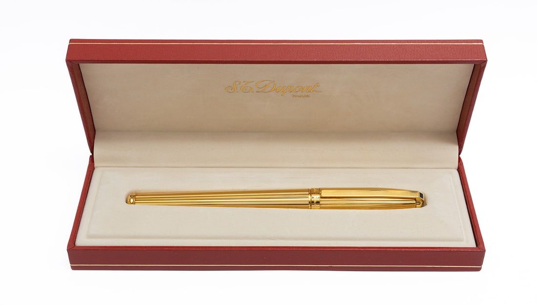 S.T. Dupont Fidelio Gold Fountain Pen, Boxed: S.T. Dupont Fidelio gold fountain pen with box, outer box and papers. Fidelio model in gold lined pattern, serial number stamped on clip, MH (hard medium) 14K nib. Length 5 1/4” and 5 3/4”