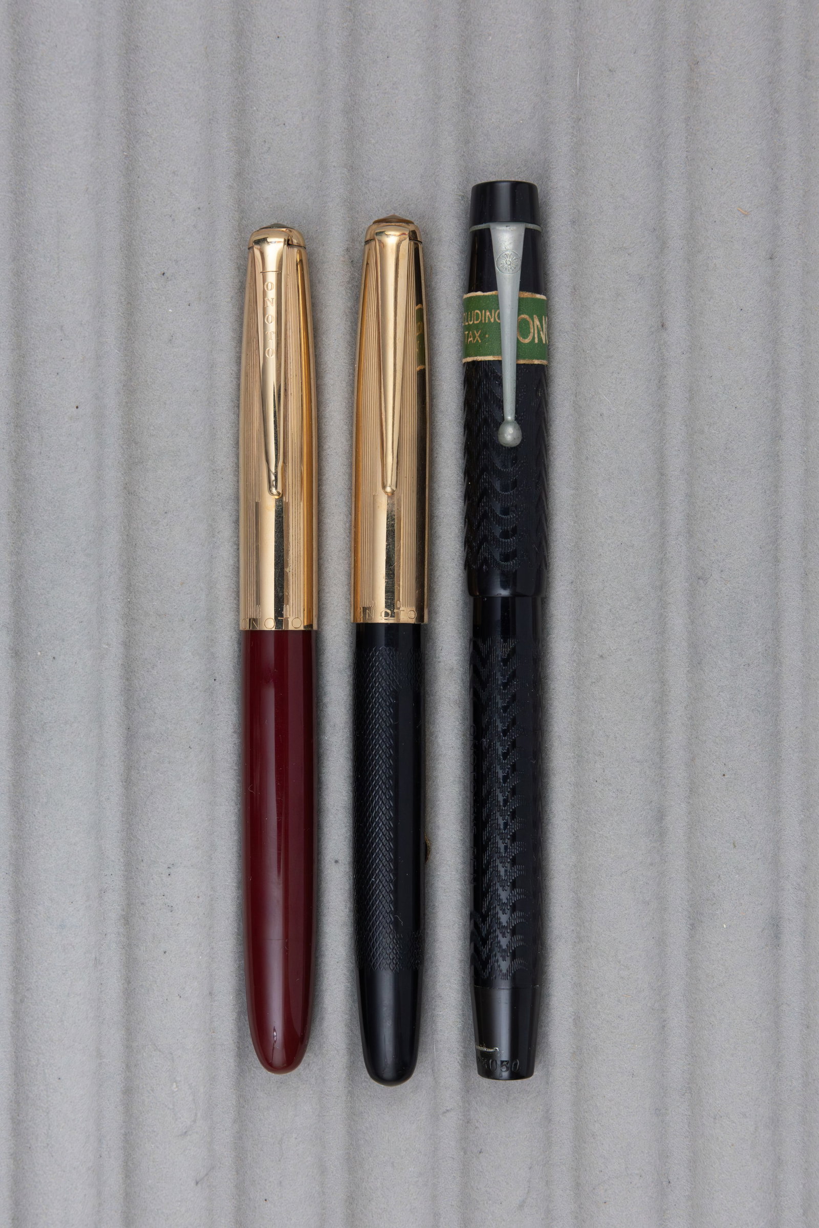 Onoto De La Rue Fountain Pens (3), Different Filling Systems: Onoto De La Rue Fountain Pens (3). Lot of three different filling systems, Onoto black chased hard rubber with original price band piston fill pen, gold filled cap lever fill pen and burgundy piston