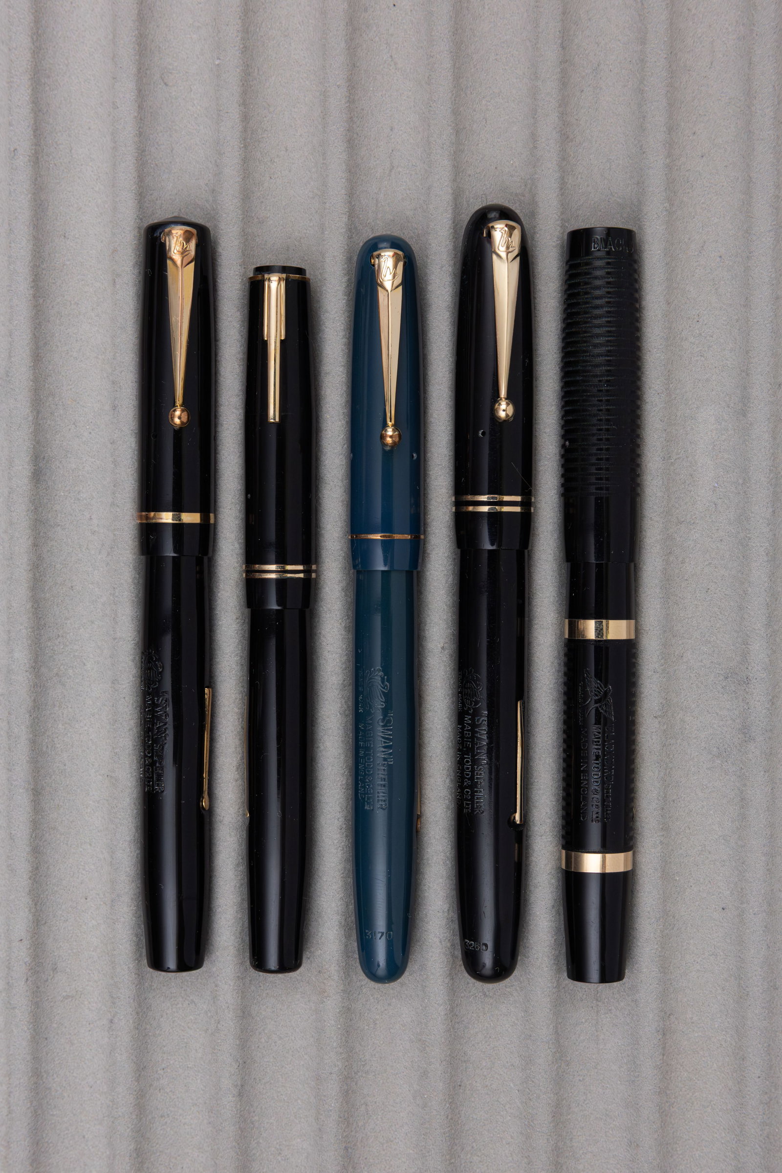 Mabie Todd Swan Fountain Pens (5): Mabie Todd Swan fountain pens (5). Black chased Blackbird clipless fountain pen by Mabie Todd along with four additional lever fill pens in black (3) and blue. All fountain pens with Swan 14K, all