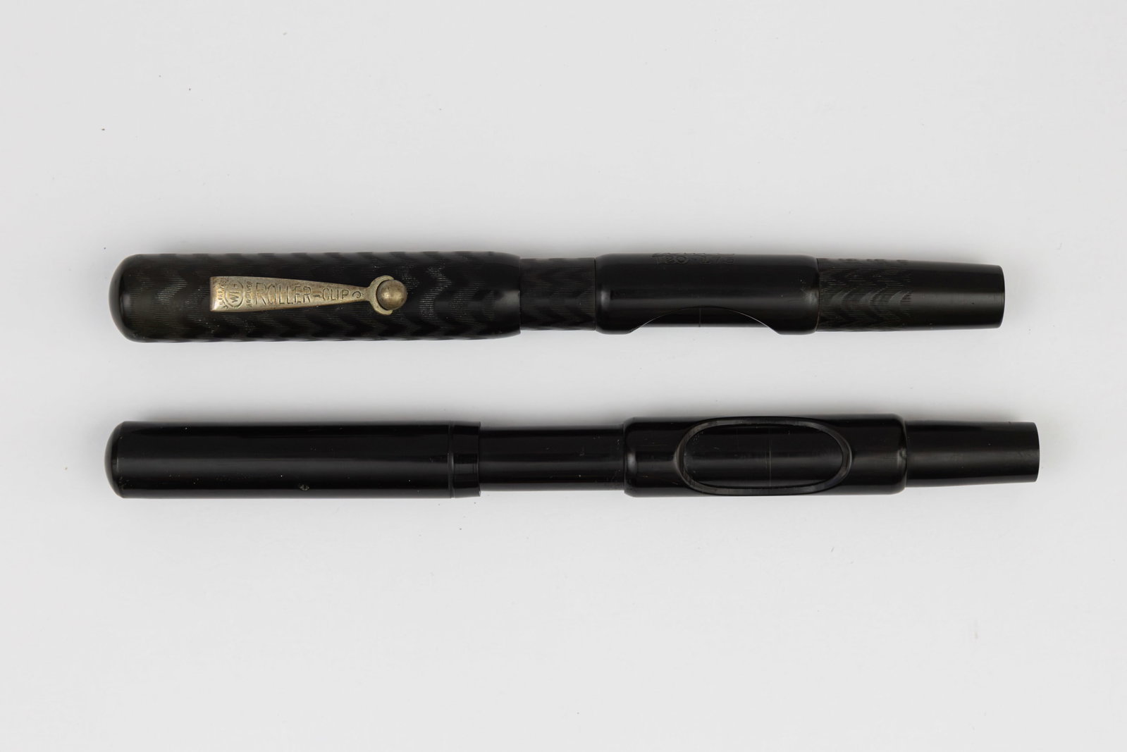 Aikin Lambert Sleeve Filler Hard Rubber Fountain Pens (2): Aikin Lambert sleeve filler smooth and chased black hard rubber fountain pens (2). Aikin Lambert black hard rubber pen marked Capital on barrel with ALCO 14K fine nib along with Todco black chased har
