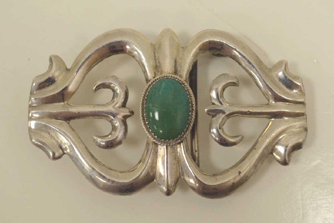 Sterling Native American style belt buckle: Sterling silver Native American style belt buckle featuring a cabochon cut turquoise mounted in the center of an open scrolling design. Measures approx. 3 1/4" x 2". Stamped on the back "M Sterling " 