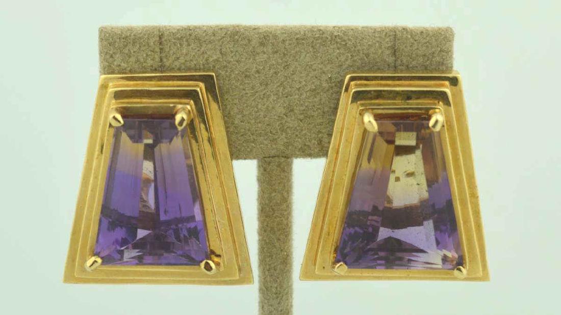 14kt yellow gold Ametrine earrings: Ladies 14kt yellow gold ametrine earrings featuring prong set free form step cut ametrine weighing approx. 32.78ct. Accented with a geometric step style frame. Finished with omega backs. Length 1". We