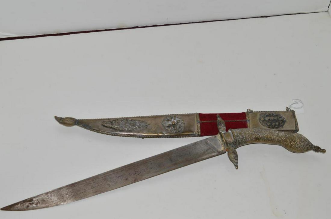Curved Brass Handled Ornate Dagger in Sheath: Curved Brass Handled Ornate Dagger in Sheath. This knife has a 13" single edged blade with script on the left side. The handle, cross guard & pommel are one piece brass construction. The sheath is woo