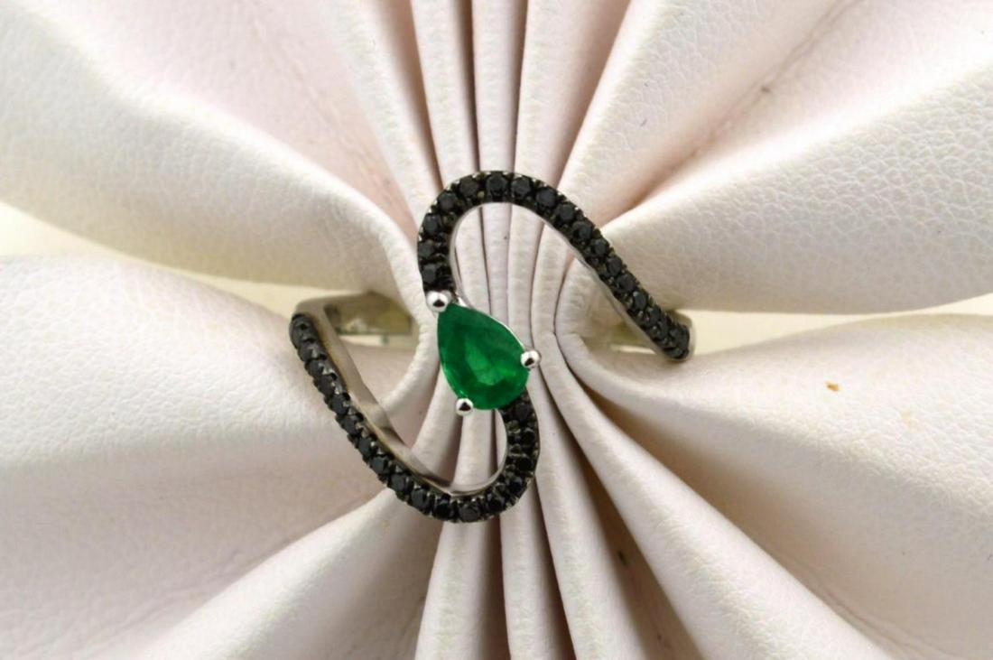 18kt white gold emerald and diamond ring: Ladies 18kt white gold emerald and diamond ring featuring a prong set pear shaped emerald weighing approx. 0.41ct.. Accented with a wave design of prong set round brilliant cut black diamonds weighing