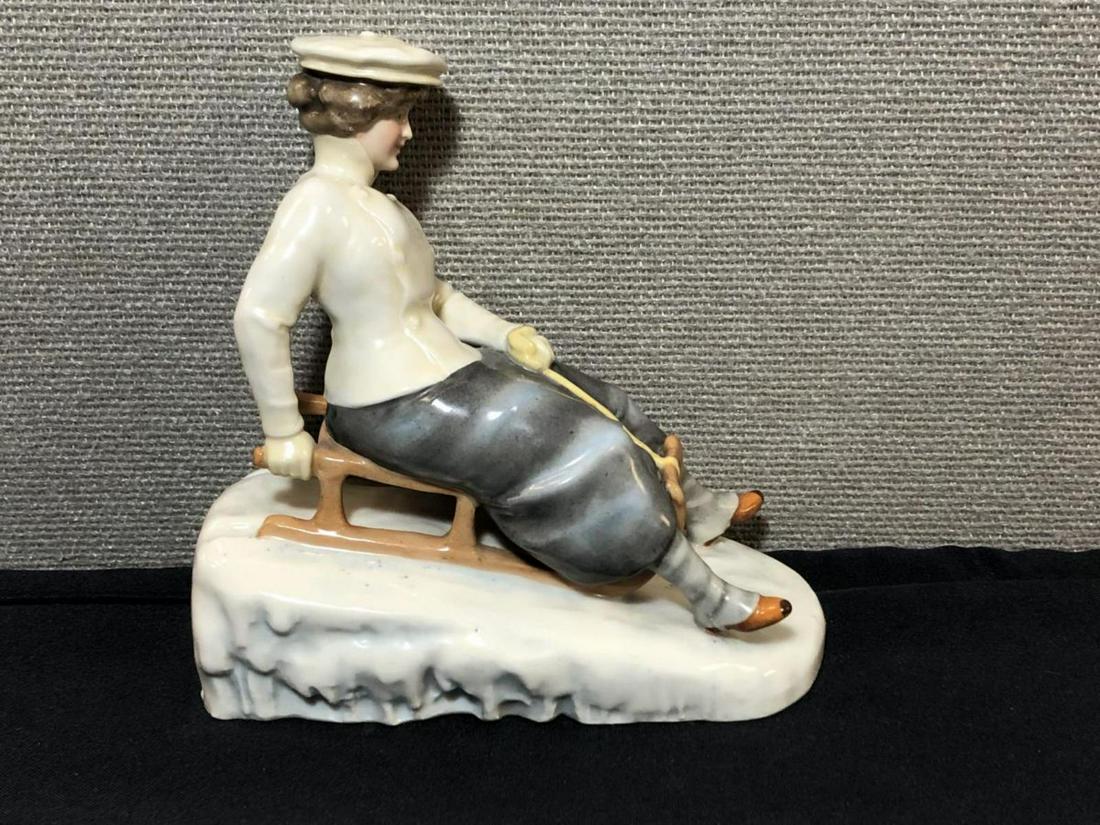 Vintage Porcelain Figurine of a Girl Sledding: A Vintage Porcelain Figurine of a Girl Sledding. Glossy finish, in excellent condition. It is marked on the underside with a 269 over 7. It has a purple hallmark of a crown over three leaves. It is 6.