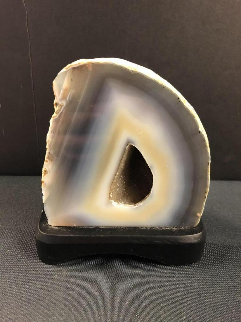 Polished & Cut Agate Geode on Stand: Polished & Cut Agate Geode on Stand. The geode is 4" x 4" and sits on a black wood base. Expertly cut and polished, revealing delicate crystal inside the hollow area.
