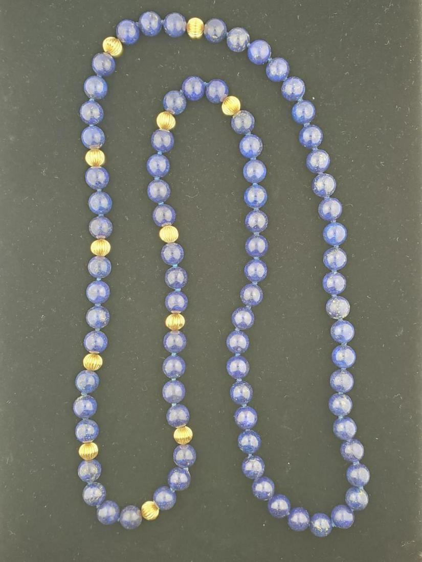 Continuous strand of lapis lazuli beads: Continuous strand of lapis lazuli beads containing single knotted lapis lazuli beads measuring approx. 10mm and separated with fluted 14kt yellow gold accent beads. Length 37”. One gold bead is slig