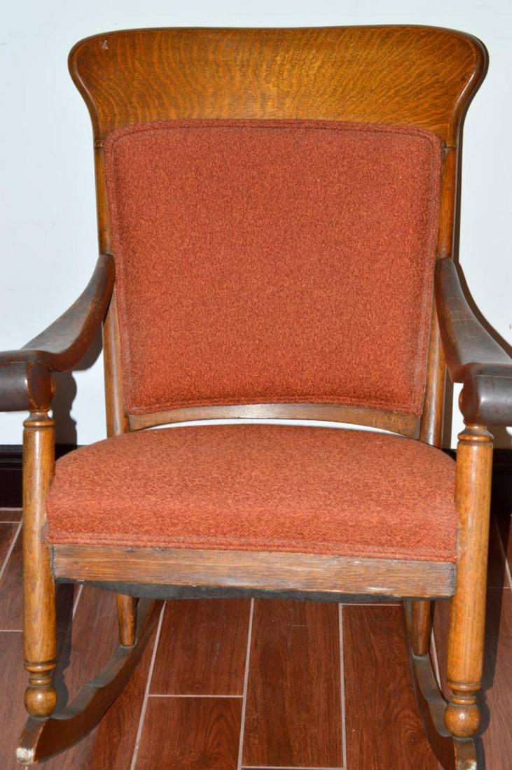 American Tiger Oak Rocking Chair circa. 1930-40's: American Tiger Oak rocking chair with upholstered back and seat. It is likely circa. 1930's or 40's. It has heavy curved arms and turned spindle legs. It is 20" between the arms and 36" tall at the ba