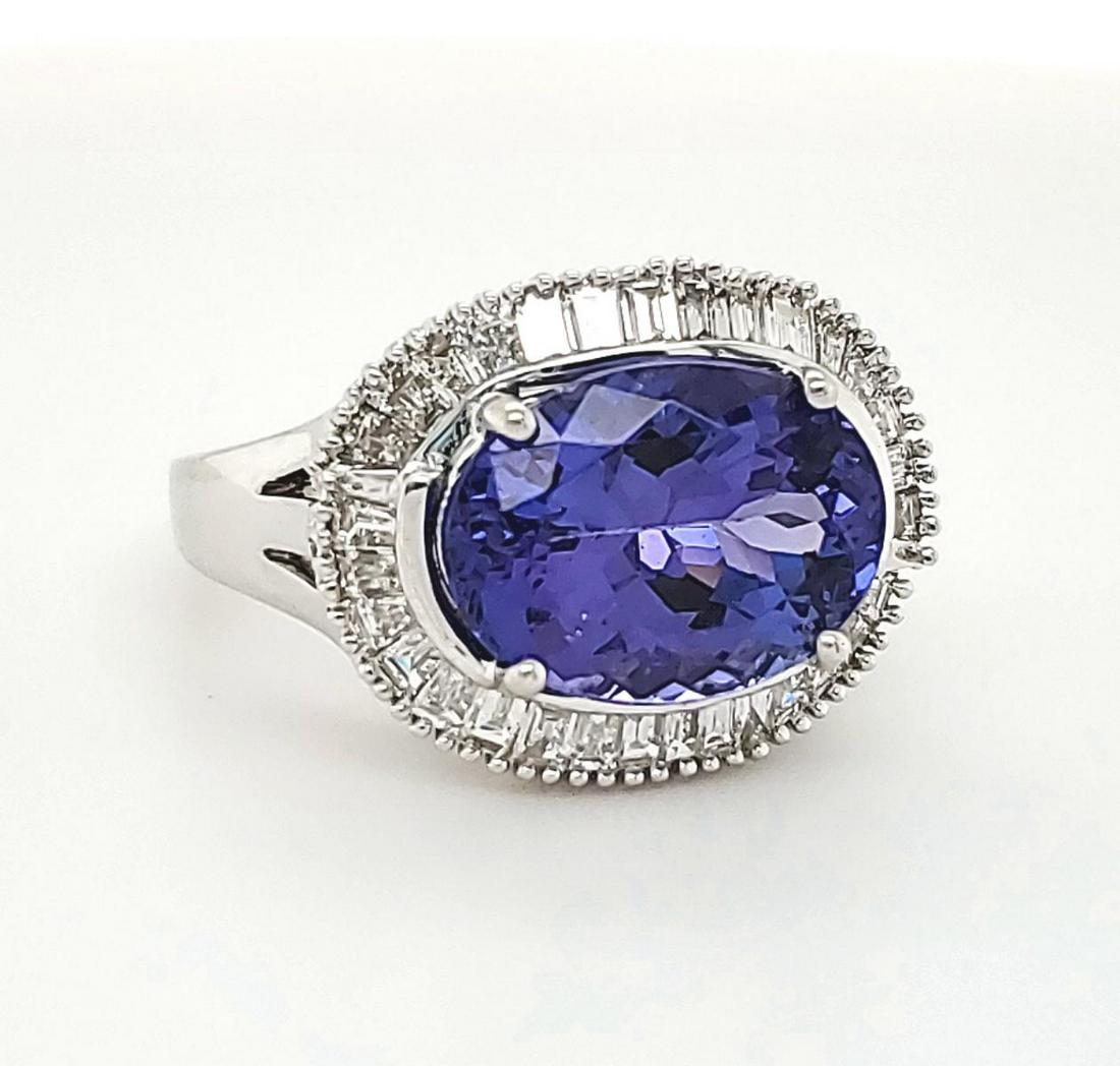 18kt white gold tanzanite and diamond ring: Ladies 18kt white gold tanzanite and diamond ring featuring a prong set oval cut medium dark, moderately strong, blue tanzanite weighing approx. 4.66ct. Surrounded by a halo of prong set baguette cut 