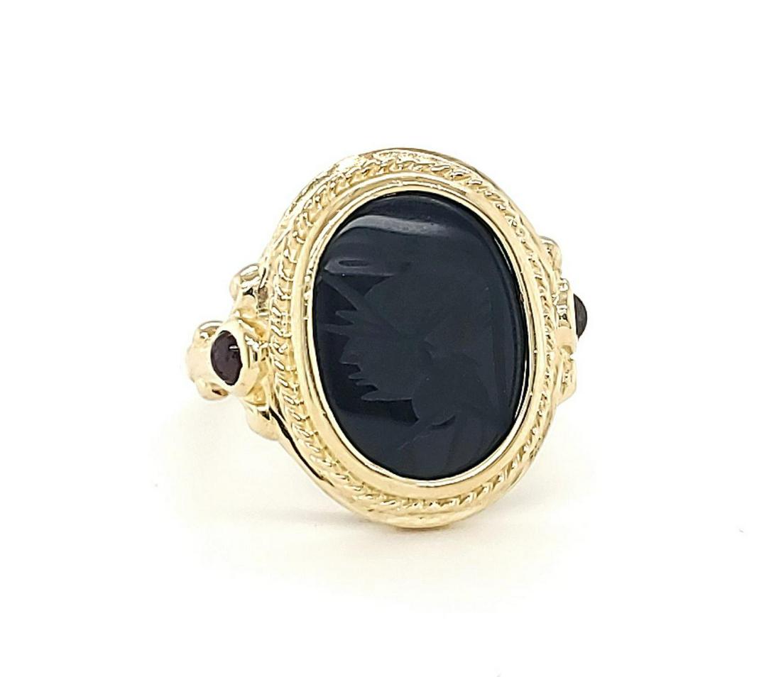 14kt yellow gold onyx intaglio ring: Ladies 14kt yellow gold onyx intaglio ring featuring an oval bezel set onyx intaglio measuring 12x12mm depicting a soldier accented with a twisted rope design and cabochon cut garnet side stones. Fing