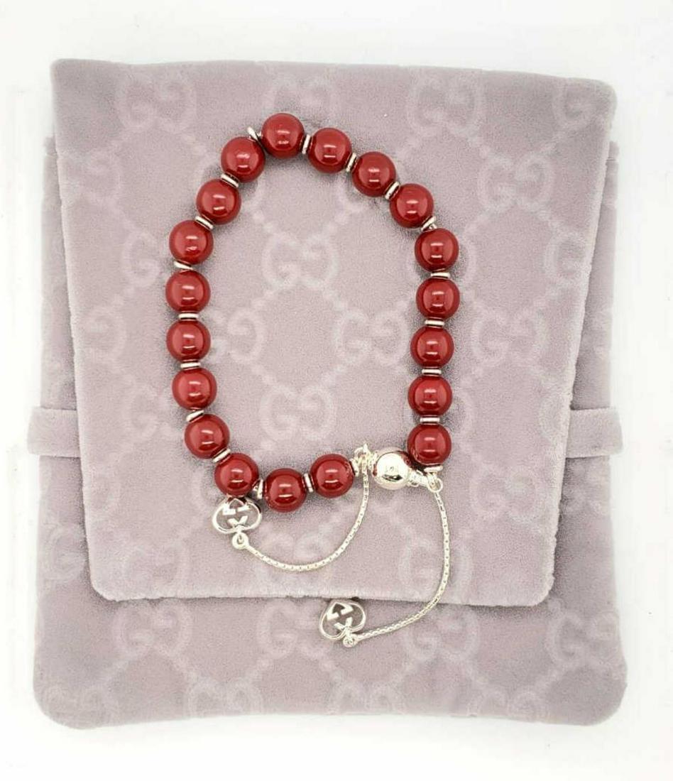 Gucci sterling & wood bead bracelet: Ladies Gucci sterling silver and varnished red wooden bead bracelet accented with dangling heart shaped Gucci logo charms. Length 7.5". Comes with the original pouch.