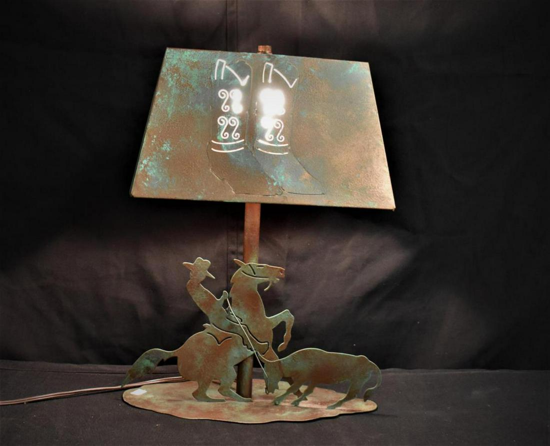 Metal Cowboy Silhouette Lamp With Metal Lamp Shade: Metal Cowboy Silhouette Lamp With Metal Lamp Shade. Stands 17 1/2" tall. Measures 13" in diameter. Cowboy boots carved on the lamp shade. The base displays a cowboy on a horse rustling a bull. Lamp in
