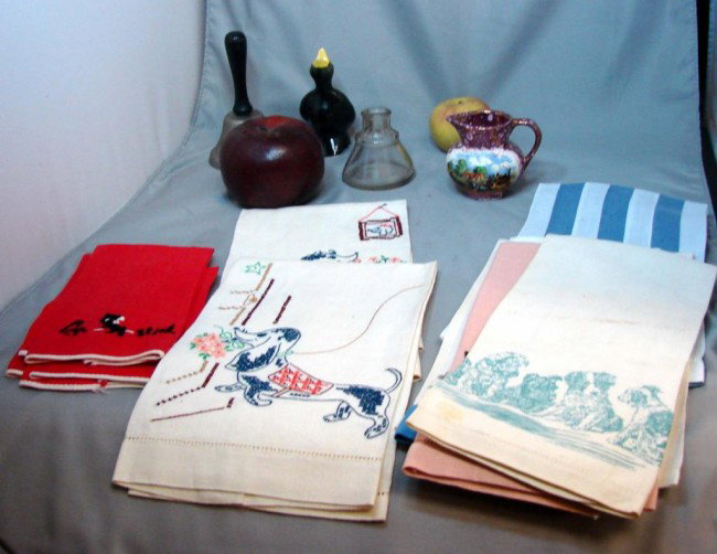 Vintage Box lot: Pie Bird, tea towels, inkwell +++: Vintage box lot consisting 13 hand embroidered tea towels, most with dog motif, wooden apple bank, wooden apple pencil sharpener, glass inkwell and a Gray's pottery pitcher.