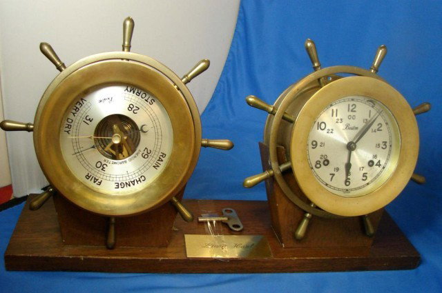 German Made Ship's Wheel Barometer & Clock: German Made Ship's Wheel Aneroid Barometer & Clock, made in Germany, marked Boston. Each weighs about 6 lbs. Mounted on wood with a plaque inscribed Long Haul.