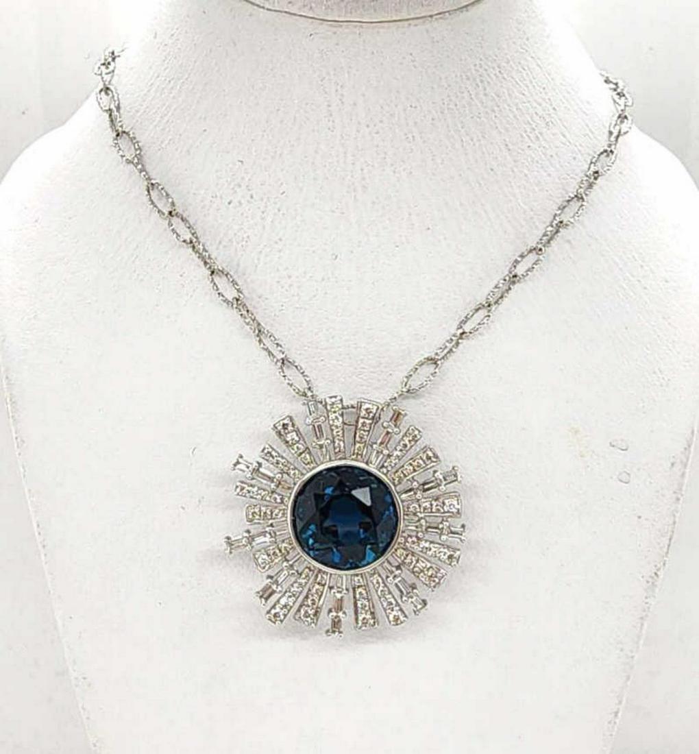 18kt blue topaz and diamond pendant by Doves: Ladies 18kt white gold blue topaz and diamond pendant by the designer Doves featuring a bezel set round London blue topaz weighing 4.54ct. Accented with a starburst frame of prong set baguette and rou