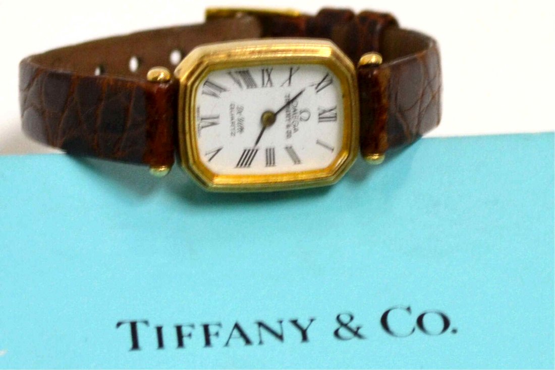 14kyg Omega DeVille Watch Tiffany & Co: Lady's 14kyg Omega DeVille watch by Tiffany & Co with octagonal case, white face with roman numbers, swiss quartz movement, push button crown and Tiffany brown leather band. 12gm