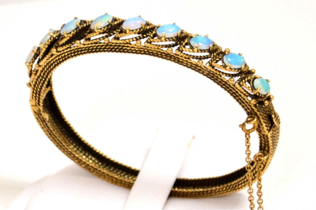 Vintage 14kyg Opal Bangle Bracelet: Lady's vintage 14kyg opal bangle bracelet with oval shaped opal, prong set, measuring 5x3.5mm, mounted at an angle with nubby gold finish and safety chain. 20.4gm