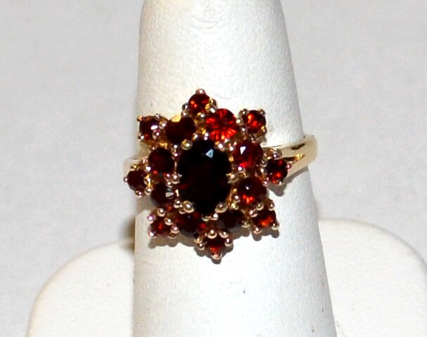 14kyg Garnet Ring: 14kyg garnet ring with one oval shaped garnet measuring 7x5mm, surrounded by 2 rows of prong set garnets, finger size 6. 4.8gm