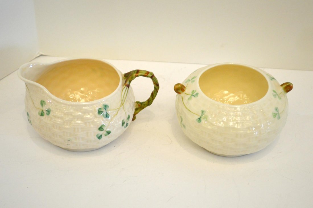 Belleek Creamer And Sugar: Belleek Creamer And Sugar. Creamer and open sugar with basket weave and clover decoration, green transfer mark, 2 1/2" and 2 3/4"h.