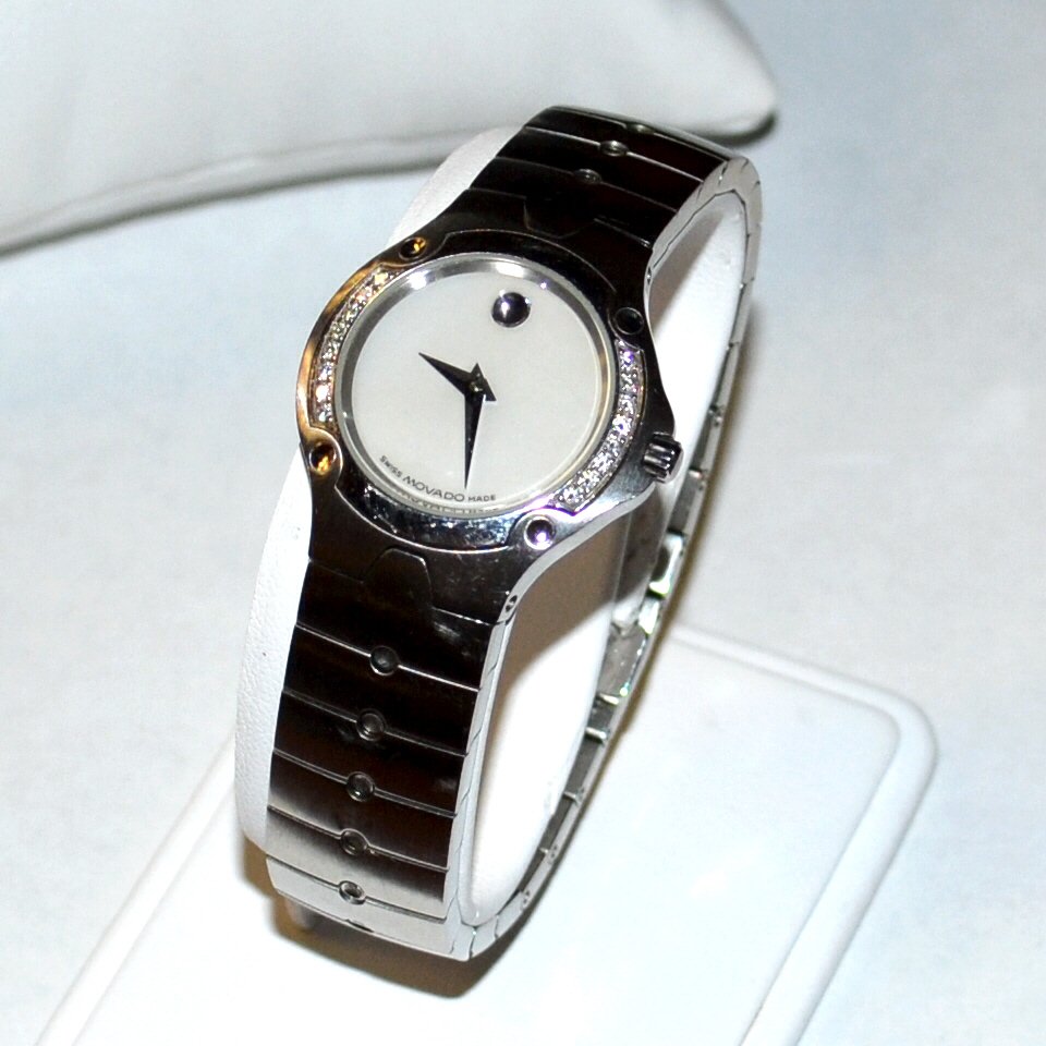 Lady's Stainless Movado Watch With Diamonds: Lady's stainless Movado diamond watch with white mother of pearl dial, Swiss movement, sapphire crystal, prong set diamonds in the bezel, water resistant and double deployment buckle.