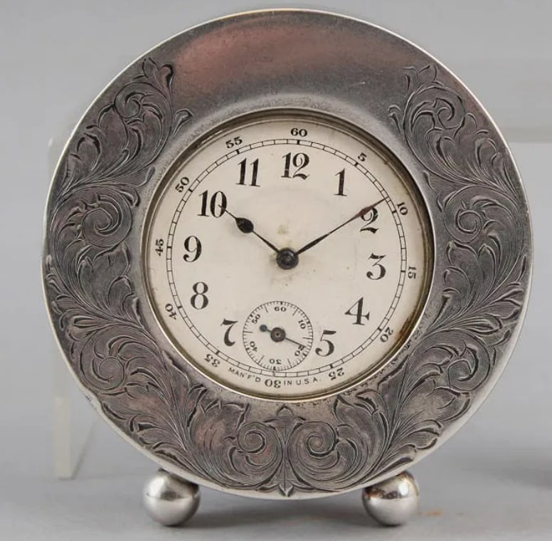 Joseph F. Fradley 19th Century Sterling Silver Desk Clock: The sterling silver frame measures 3" in diameter by 5/8" deep and stands on two small ball feet. There is engraved acanthus leaf scrollwork around the frame with a vacant cartouche at the top that ha