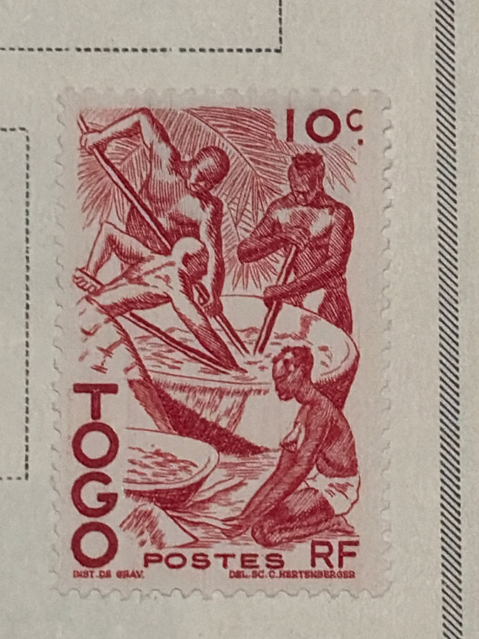 Vintage Togo 10-Centime Labor Scene Stamp: Vintage red 10-centime Togo postage stamp featuring two seated figures and an occupational or labor scene. The nearby black-and-white stamp image and empty spaces are printed elements of the album pag