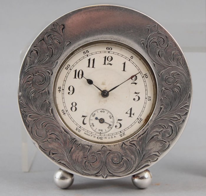 Joseph F. Fradley 19th Century Sterling Silver Desk Clock: The sterling silver frame measures 3" in diameter by 5/8" deep and stands on two small ball feet. There is engraved acanthus leaf scrollwork around the frame with a vacant cartouche at the top that