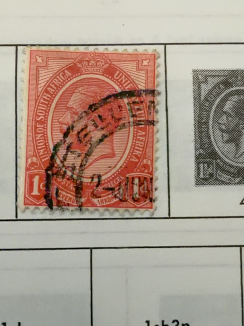 South Africa King George V One-Penny Stamp: Vintage Union of South Africa one-penny red-orange postage stamp featuring King George V. Used example with prominent circular postal cancellation, perforated edges and age-related wear; mounted on