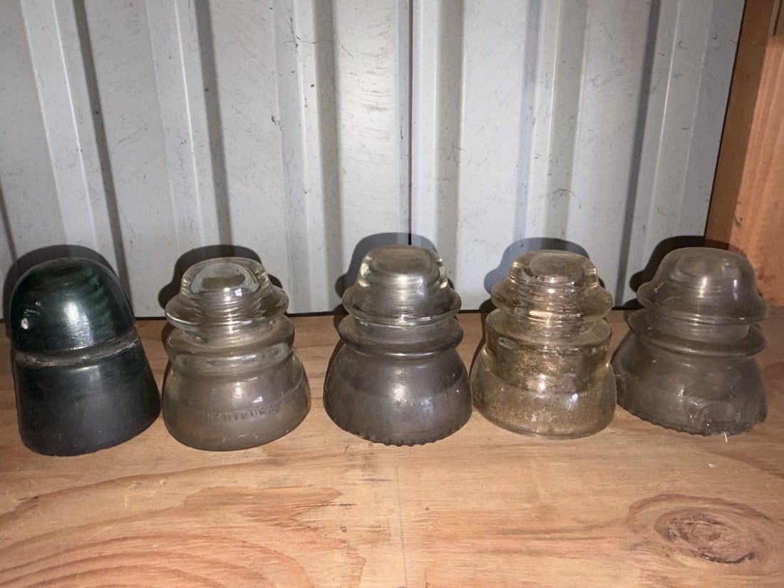 Antique Glass Utility Insulators Collection ? 5 Pieces: Group of five antique glass telegraph, telephone and electrical utility insulators in clear, smoky and green glass. Various shapes and manufacturers with embossed markings visible on several examples.