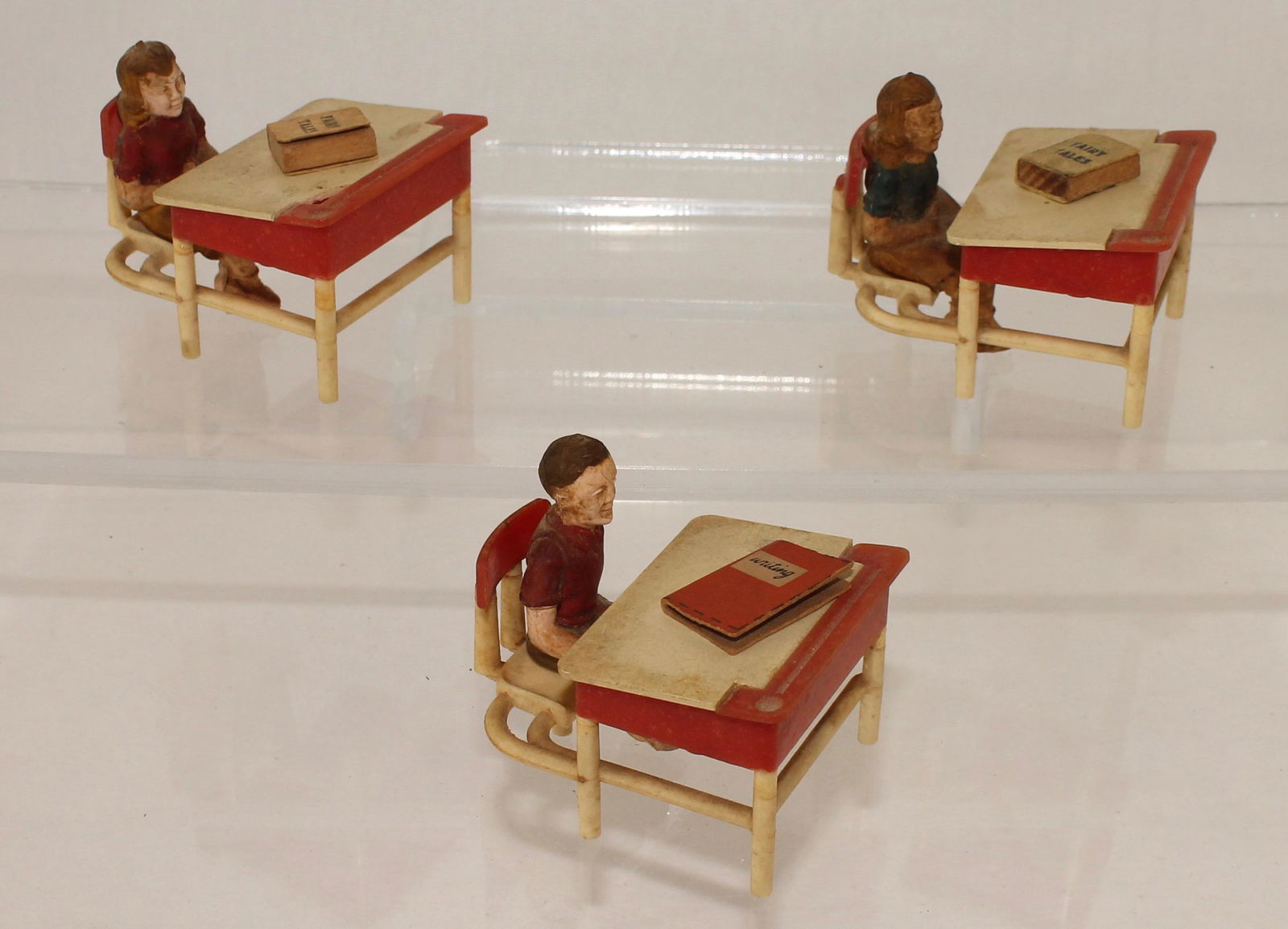 Lot of Plastic School Desks with Students: Plastic School Desks with Students and Books. Lot includes 3 School Desks with Seated Students and Books by an Unknown Maker. Figures are 60mm and made of Plastic. Pieces are soiled and show age. 9 Pi