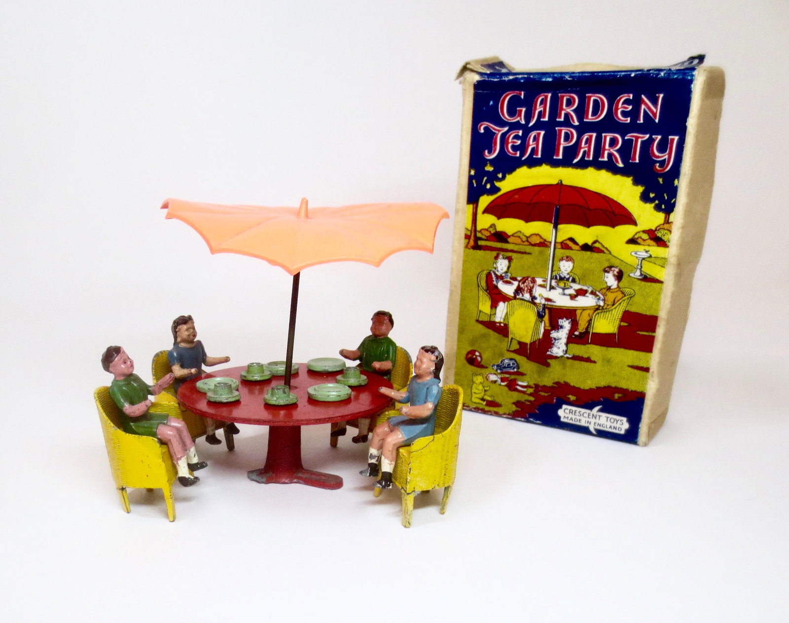 Crescent Garden Tea Party Set: Four children gathered around a table for an afternoon tea party. 18 pieces. Good to fair condition (table missing one leg, some cracks, chair repairs, and warped umbrella). Box in good condition (one