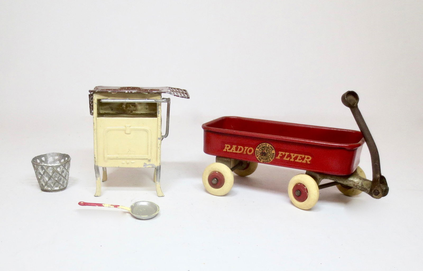 American Dimestore Toys: Tin Dollhouse Stove, Skillet and Waste Basket. Plus an iron Radio Flyer Wagon. Measure 1" to 4" long. 4 pieces. Excellent to very good condition. Unboxed.