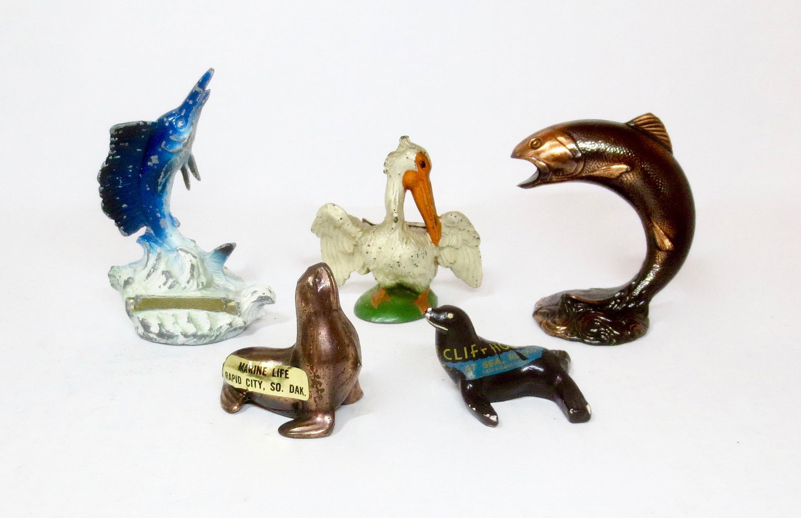 Vintage Beach Vacation Souvenir Figures: Marine Life Rapid City South Dakota metal cast Seal, Cliff House San Francisco wooden Seal, Bronze Jumping Trout, Miami lead Pelican, and lead Jumping Marlin. 1" tall to 3-1/2" tall. 5 pieces. Excelle