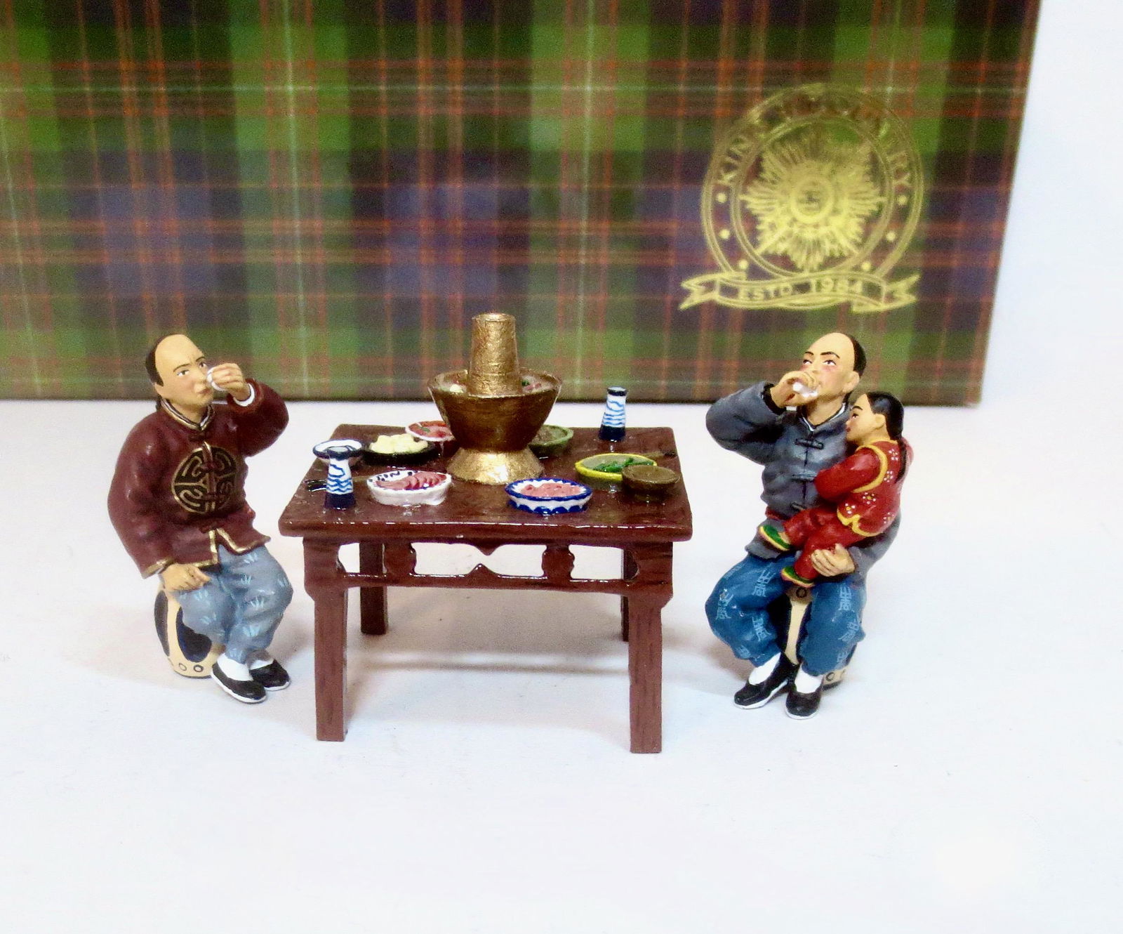 King & Country #HK133(M) Wine Shop Customers: Two seated Chinese gentlemen, one holding his young son, enjoying a convivial cup of wine. In front of them a table groaning under a selection of traditional Chinese “hot-pot” dishes. Retired set.