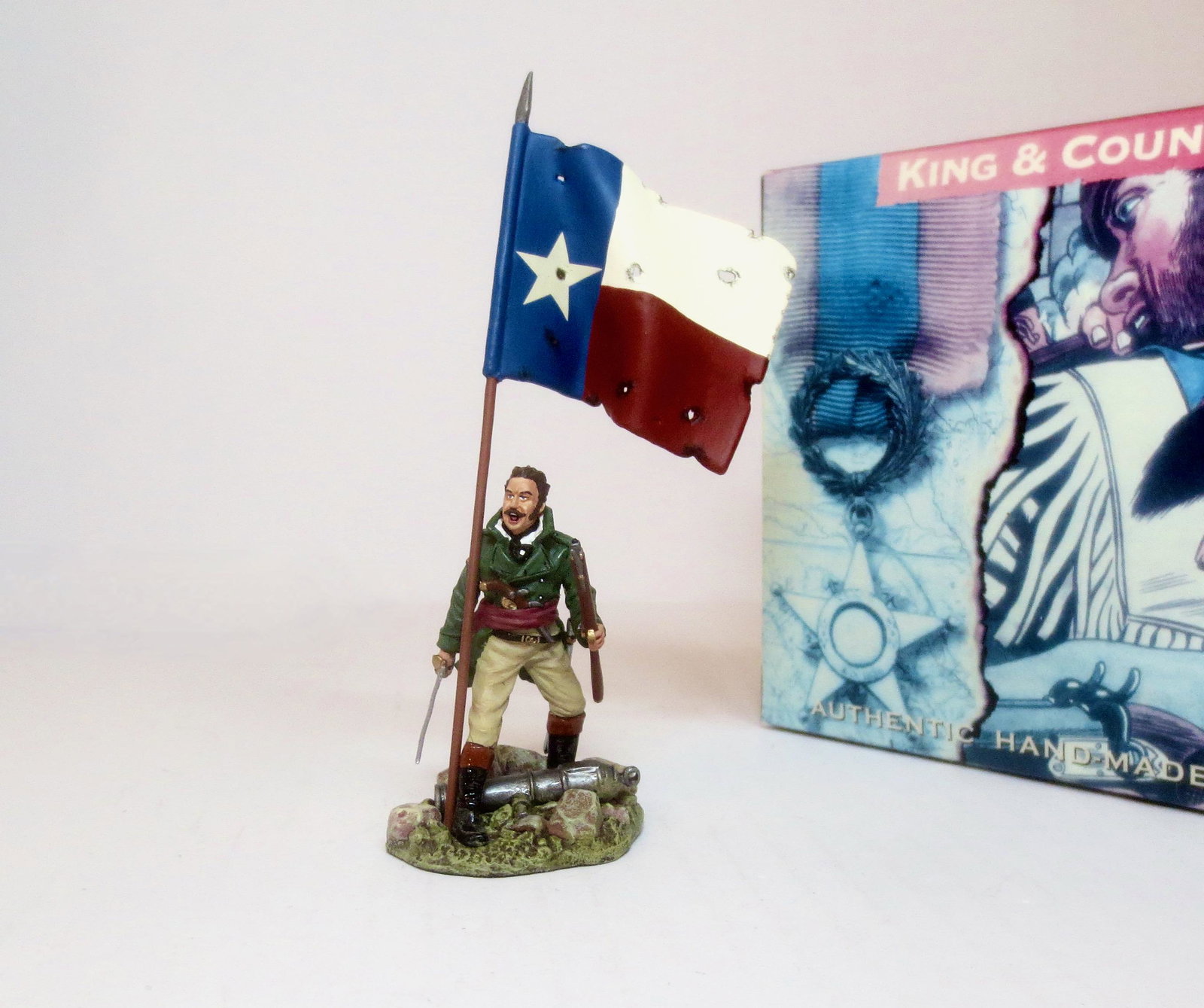 King & Country #RTA033A “James Butler Bonham”: Bonham stands defiantly, sword in one hand, rifle in the other supporting the “1824” Republic of Texas Flag. 2 pieces. Mint condition. Box excellent.