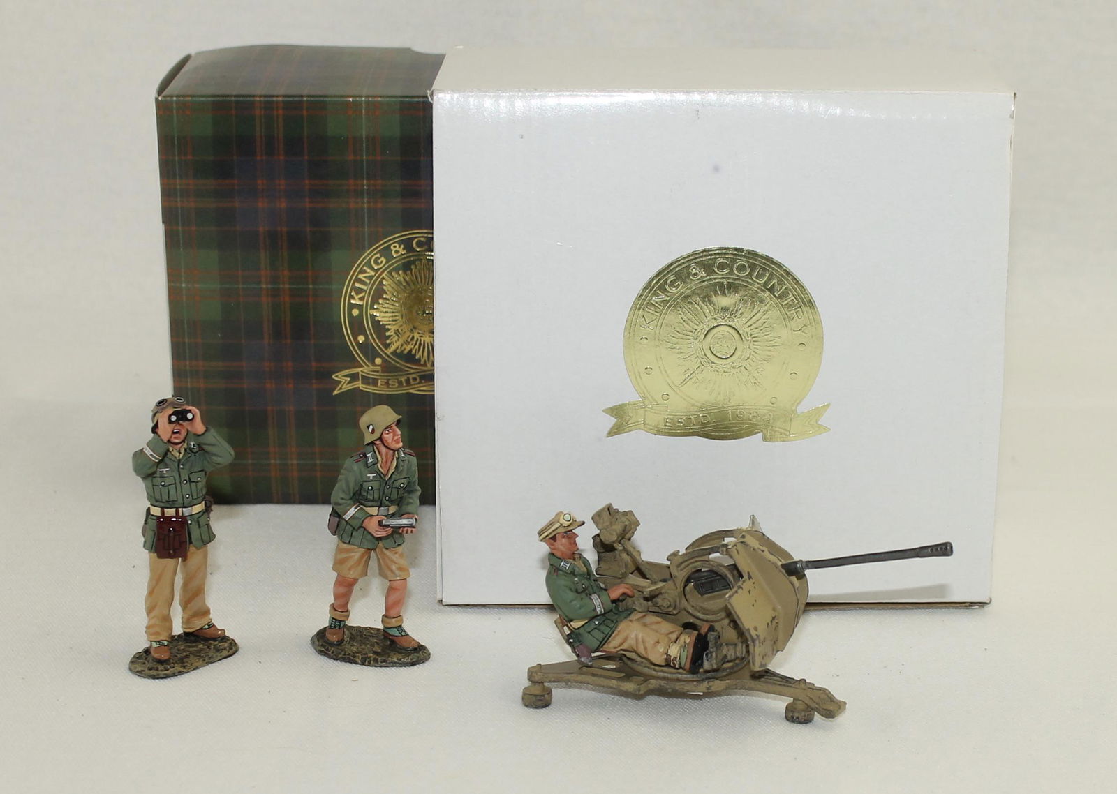King & Country Lot 20mm Flak Gun and Crew: German Afrika Korps. Lot includes Set #AK095 Flak Gun with Seated Gunner and Set #Ak096 Flak Gun Crew. 4 Pieces. Condition Very Good. Gun Barrel Slightly Bent. Armor Shield Broken at Supports. Boxes V